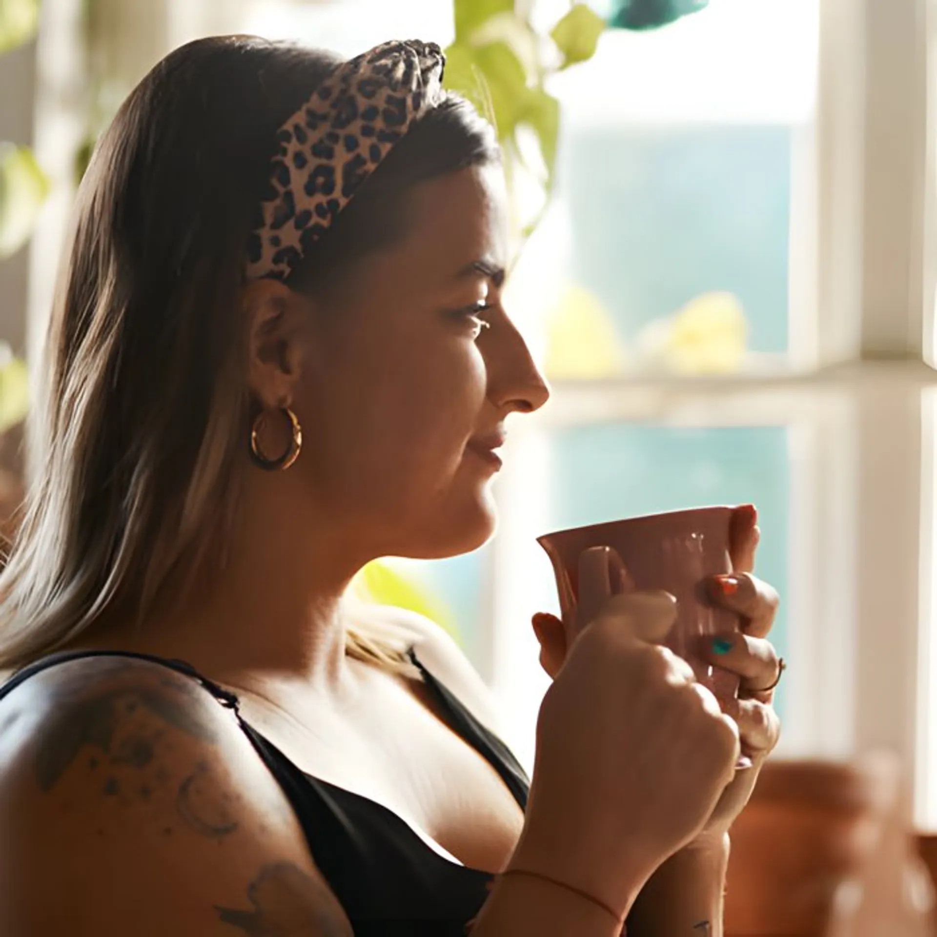 Woman with a cup of coffee at a plant-filled window
