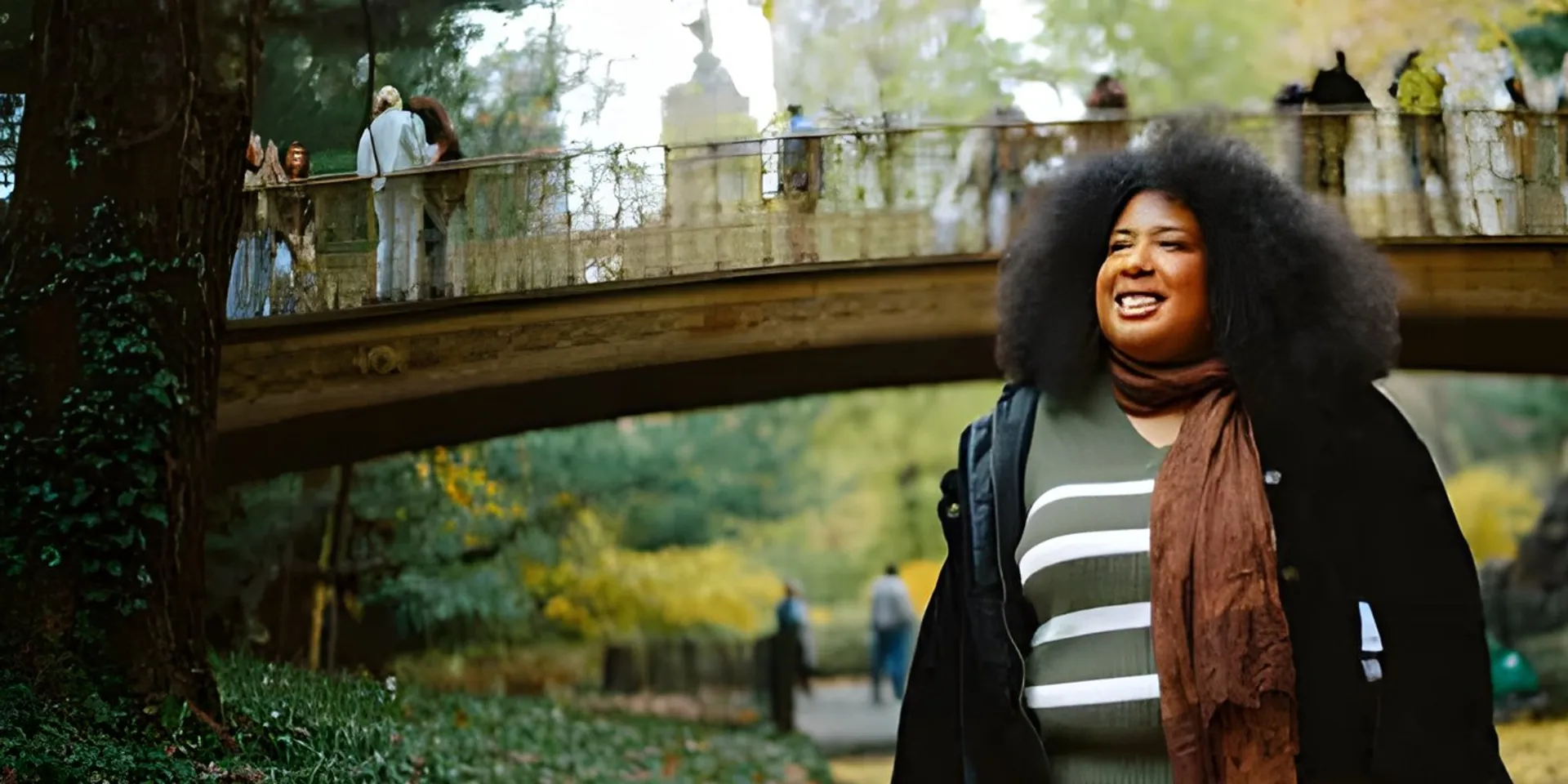 Woman strolling under autumn trees by a park bridge